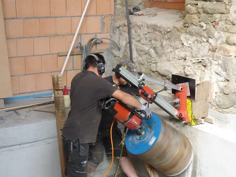 Core drilling crew running a rig-mounted diamond core drill on a concrete wall